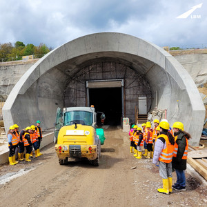 Ausschnitt mit Blick auf eine Tunnelröhre im Baustellenzustand, in gelben Gummistiefeln, mit orangener Warnweste und mit gelben Arbeitshelmen steht dort eine Gruppe junger Mädchen und besichtigt die Baustelle des Tunnels in Bad Bergzabern