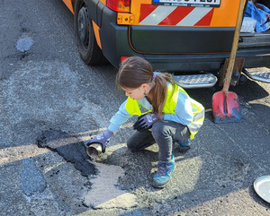 Schülerin repariert kleine Fahrbahnschäden.