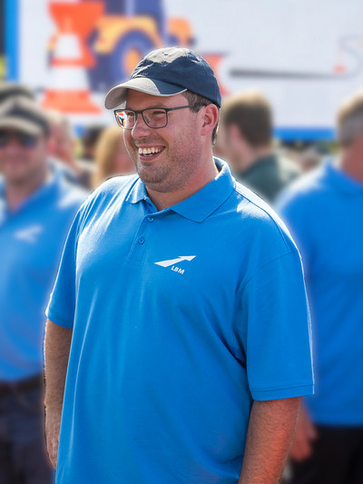 Ein Mann in einem blauen LBM-Poloshirt und mit einer dunkelblauen Kappe lacht.