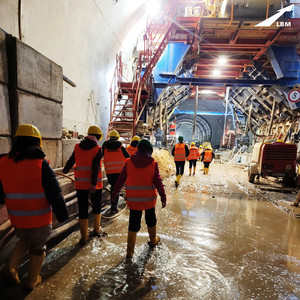 Ausschnitt mit Blick in eine Tunnelröhre im Baustellenzustand, in gelben Gummistiefeln, mit orangener Warnweste und mit gelben Arbeitshelmen läuft dort eine Gruppe junger Mädchen und besichtigt die Baustelle des Tunnels in Bad Bergzabern