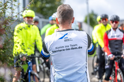 Ein Mann im LBM-Shirt fotografiert eine Gruppe Radfahrer.