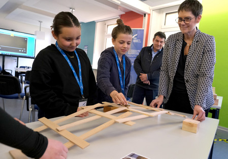 Zusammen mit der Staatssekretärin bauen die Mädchen die Leonardo-Brücke aus Holzstäbchen.