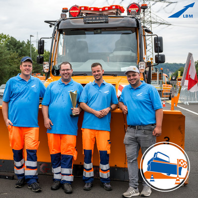 Die beiden LBM Teams bei der Deutschen Meisterschaft im Schneepflugfahren 2023 in Koblenz strahlen nach der Meisterschaft vor dem Unimog mit Pokal in die Kamera.