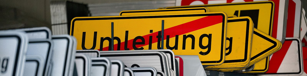 Verschiedene Verkehrszeichen. Im Fokus steht ein Umleitungsschild. Drumherum befinden sich weitere Verkehrsschilder. Diese sind unscharf und befinden sich im Hintergrund.