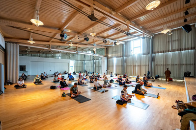 Mehrere Menschen machen in einer Halle Yoga.