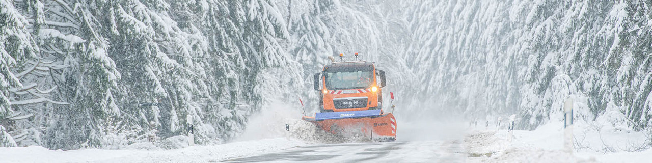 orangenes Winterdienstfahrzeug auf einer Straße im Wald