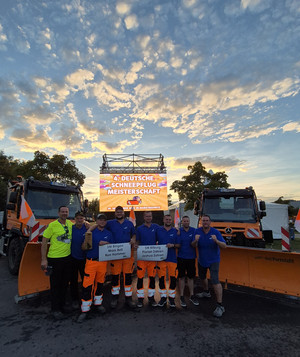 Das Team steht mit dem Betreuerstab vor zwei Unimogs. 