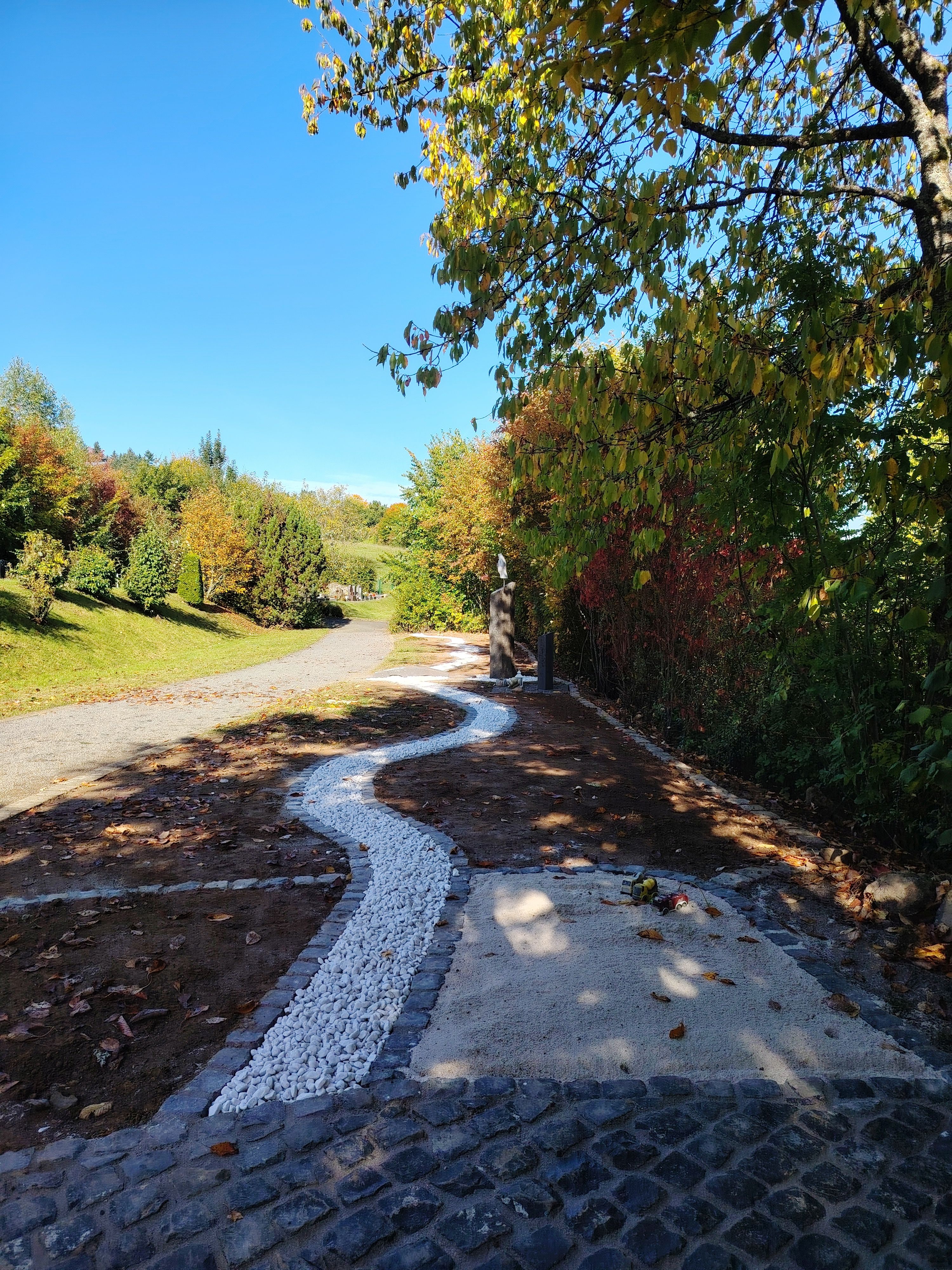 Die Azubis haben eine bereits bestehende, aus Schotter angedeutete Wasserfläche, wellenförmig entlang der Gräber weitergeführt. 