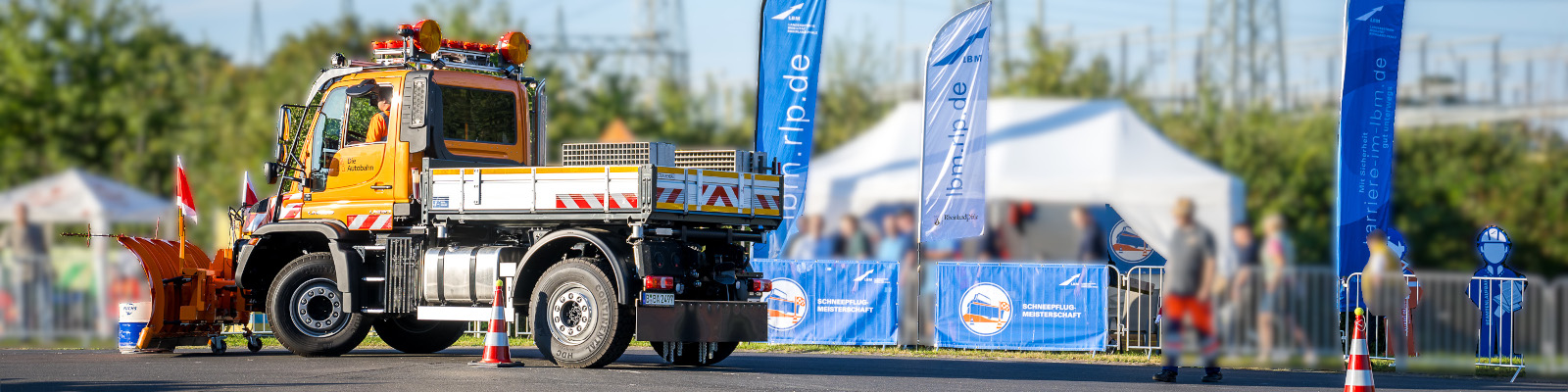 Blick auf das LBM-Zelt bei der Deutschen Meisterschaft im Schneepflugfahren 2023 in Koblenz, davor ein Unimog, der den Parcours absolviert.