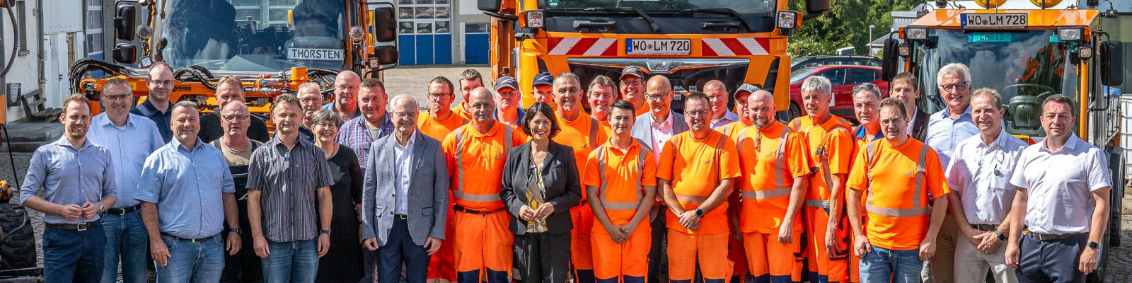 Eine Gruppe von Menschen steht vor geparkten Straßenfahrzeugen in einem Innenhof.