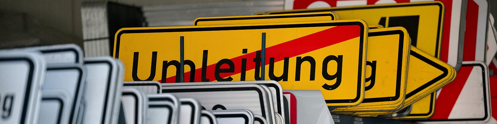 Verschiedene Verkehrszeichen. Im Fokus steht ein Umleitungsschild. Drumherum befinden sich weitere Verkehrsschilder. Diese sind unscharf und befinden sich im Hintergrund.